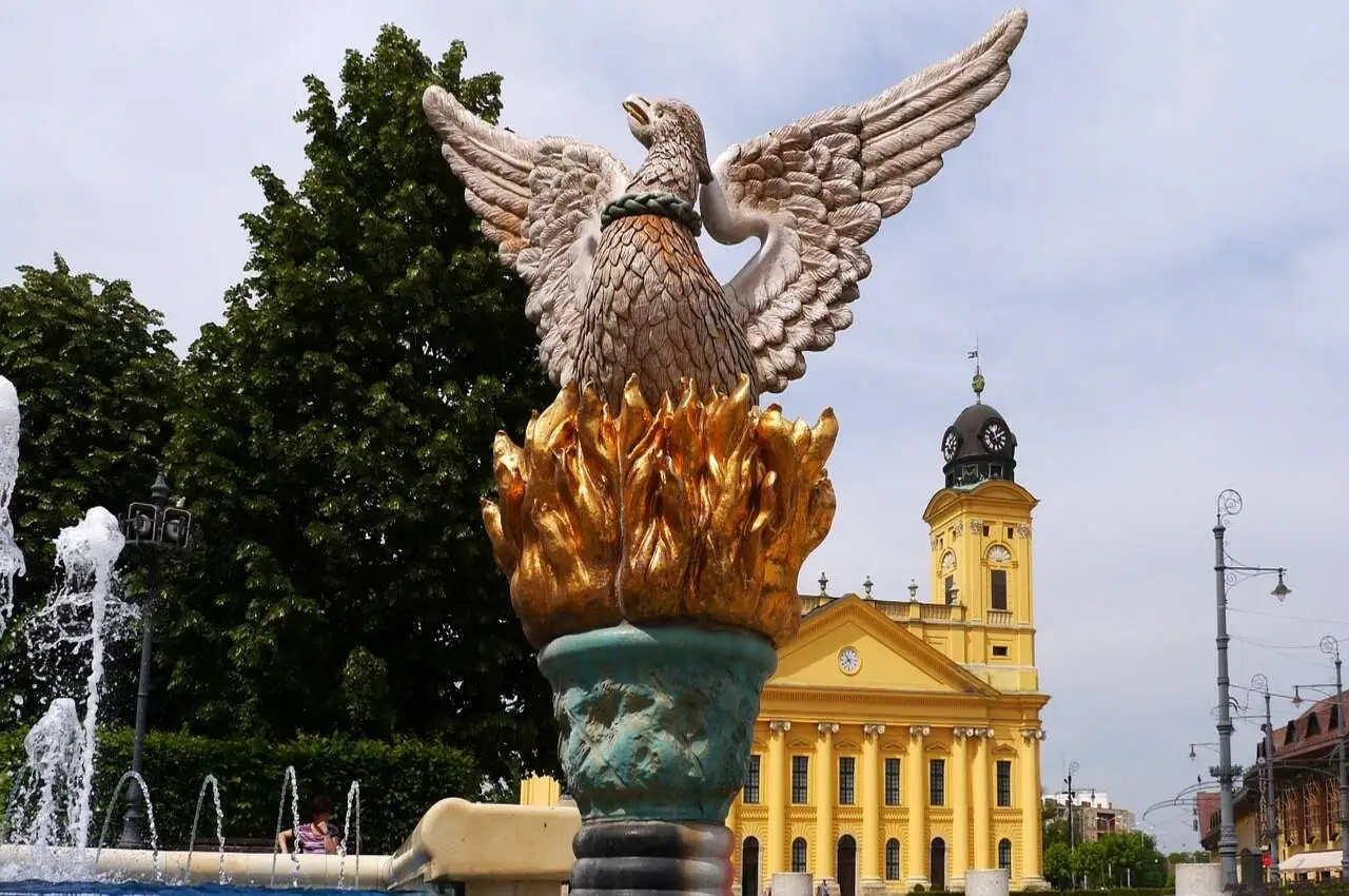 A falcon statue with a building on the back in Debrecen