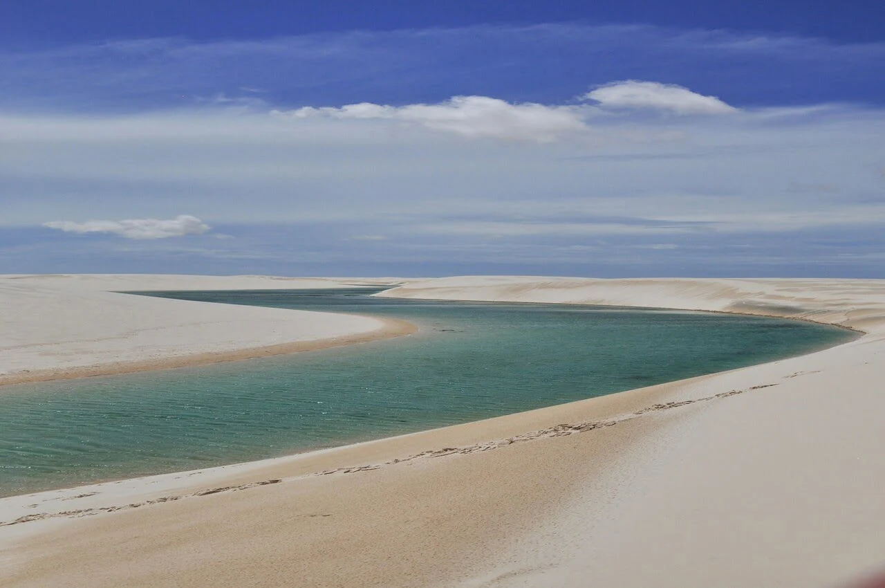 a river running through a sandy area with Lençóis Maranhenses National Park in the background