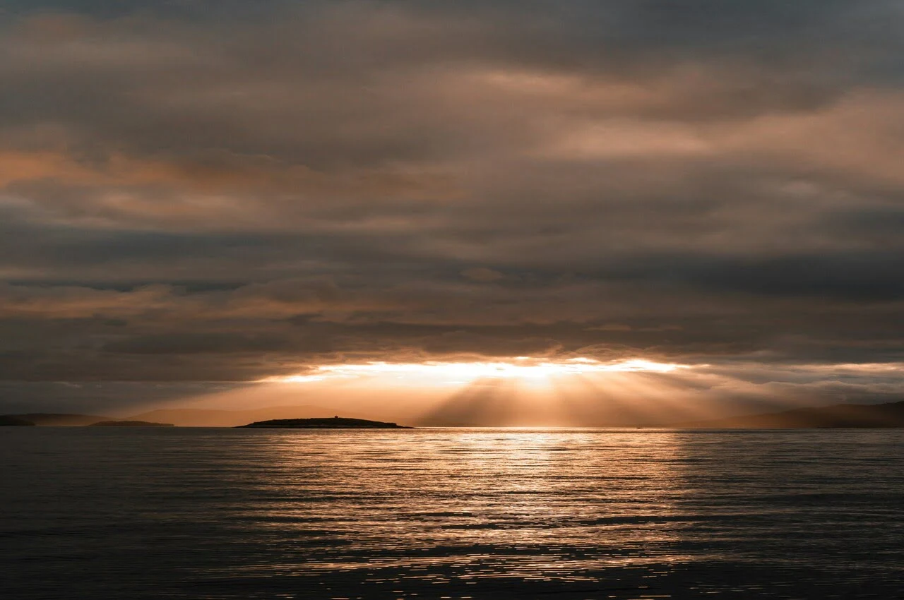 sun shining through the clouds over a body of water