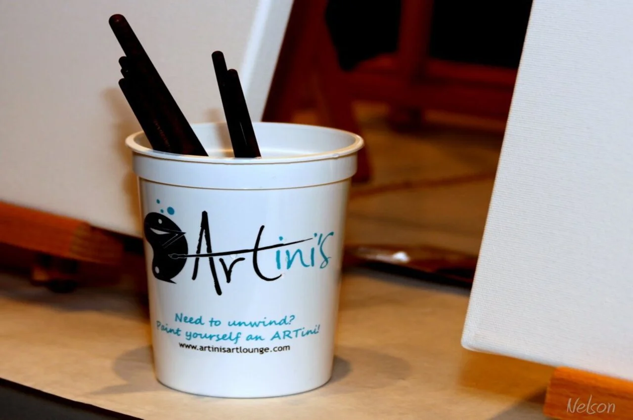 A cup with paint brushes with Artinis written on it.