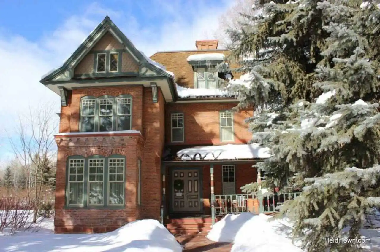 An old Queen-Anne-style house with a tree in front covered with snow.