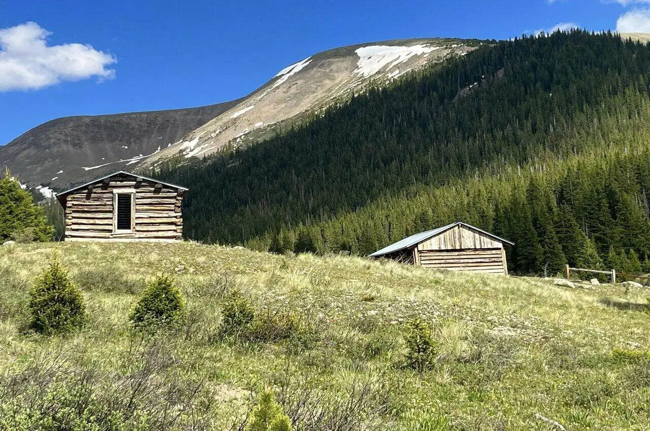 Two wooden houses with two mountains on the back.